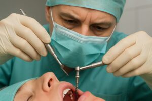 A dental surgeon carefully places an endosteal implant into a patient's jawbone, ensuring precise placement for optimal integration. No text on image.